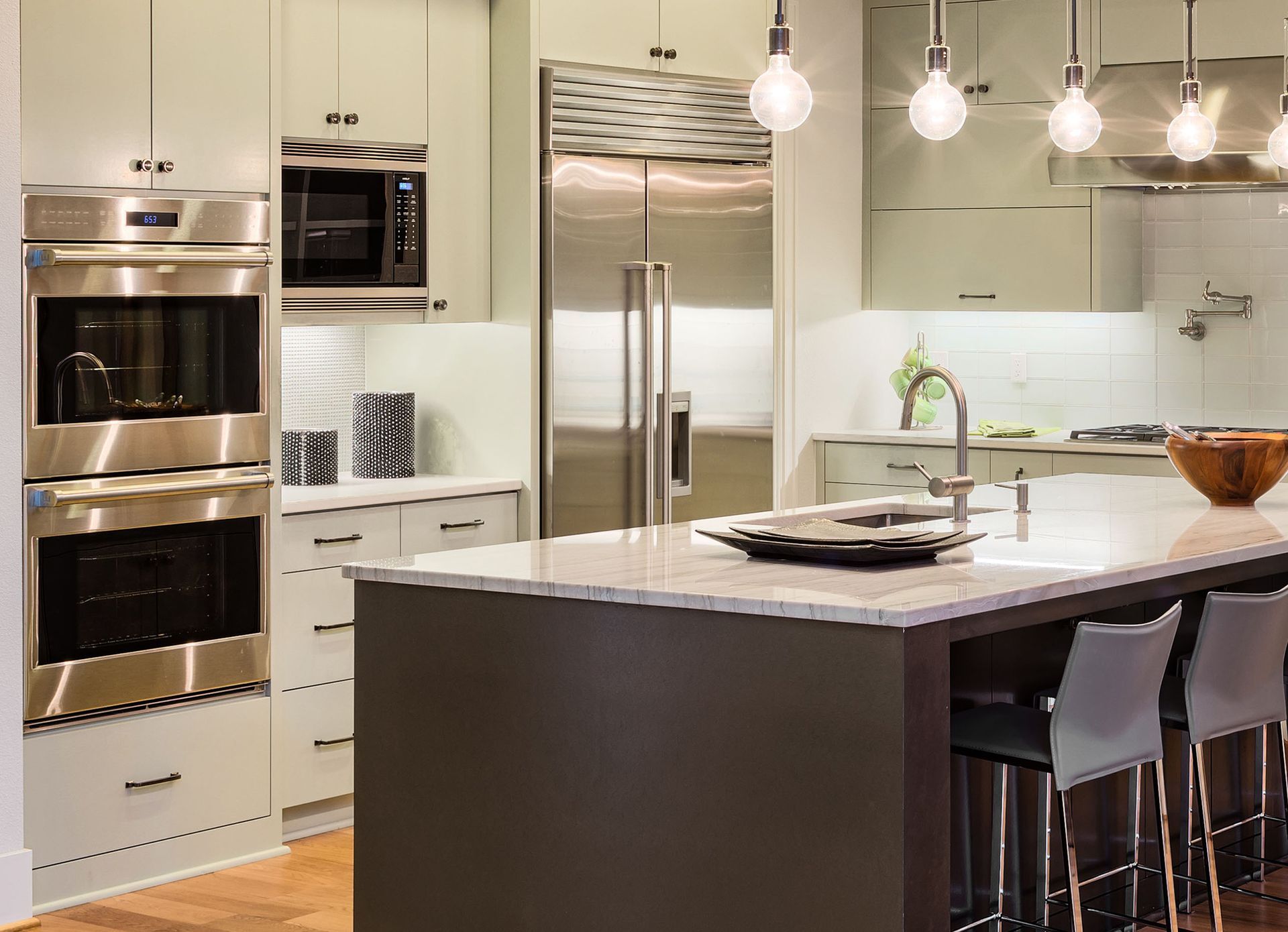 Modern kitchen with stainless steel appliances, light cabinets, and a dark island with bar stools.