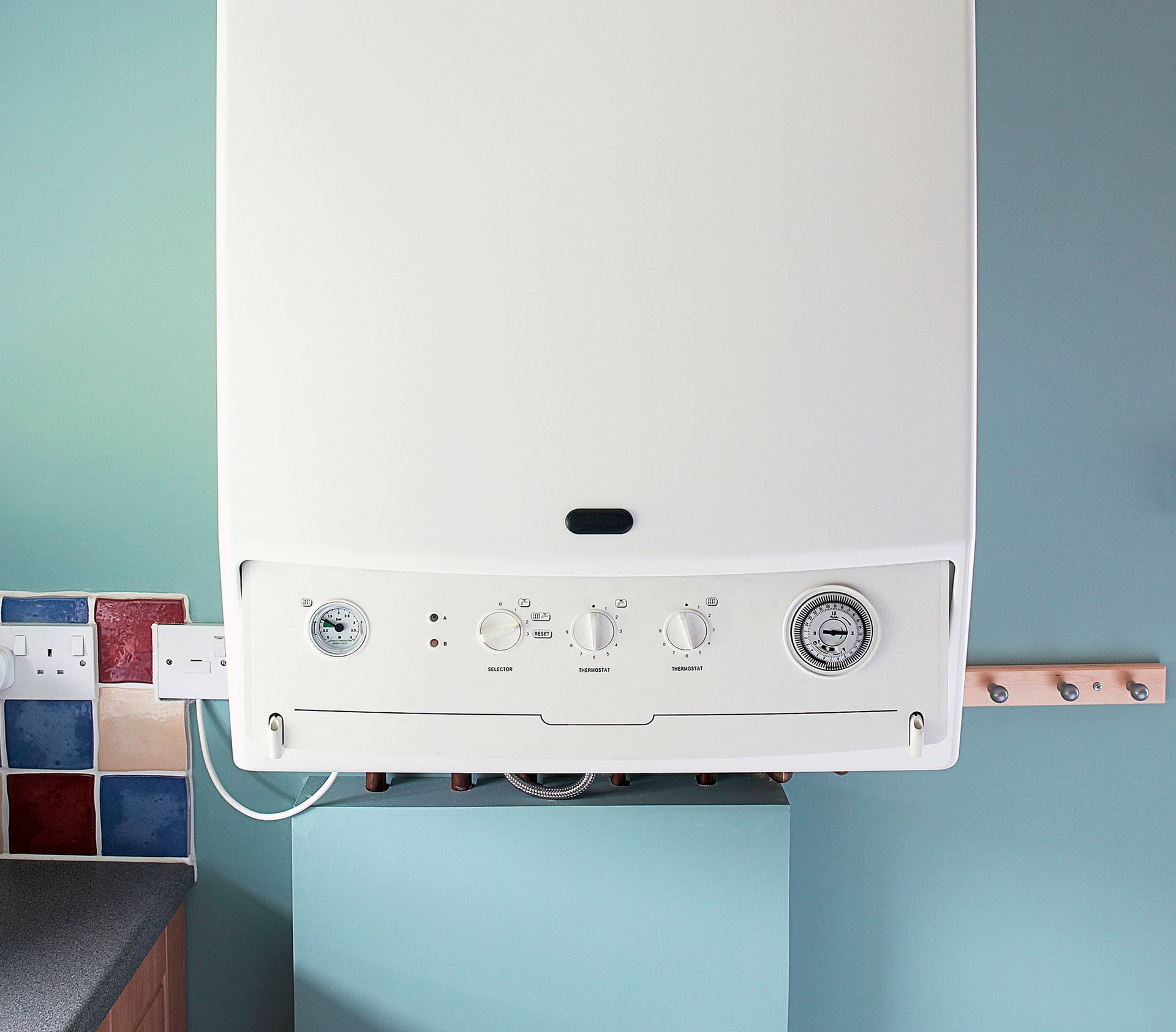 White boiler unit mounted on a light blue wall, with dials and a pressure gauge.
