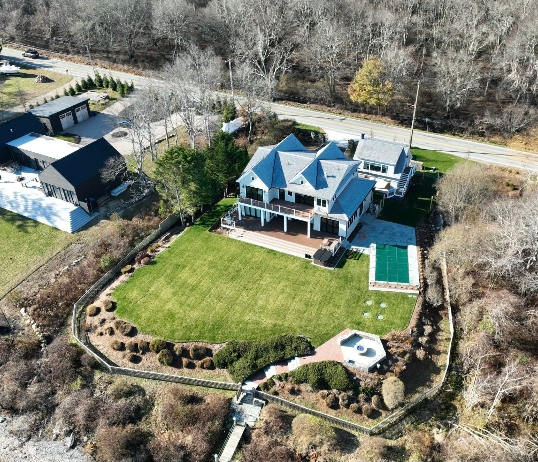 Aerial view of a large white house with a pool, green lawn, and surrounding greenery.