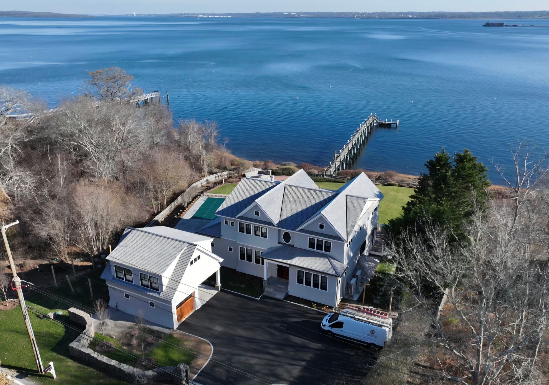 Aerial view of a large gray house with a dock on a blue bay.