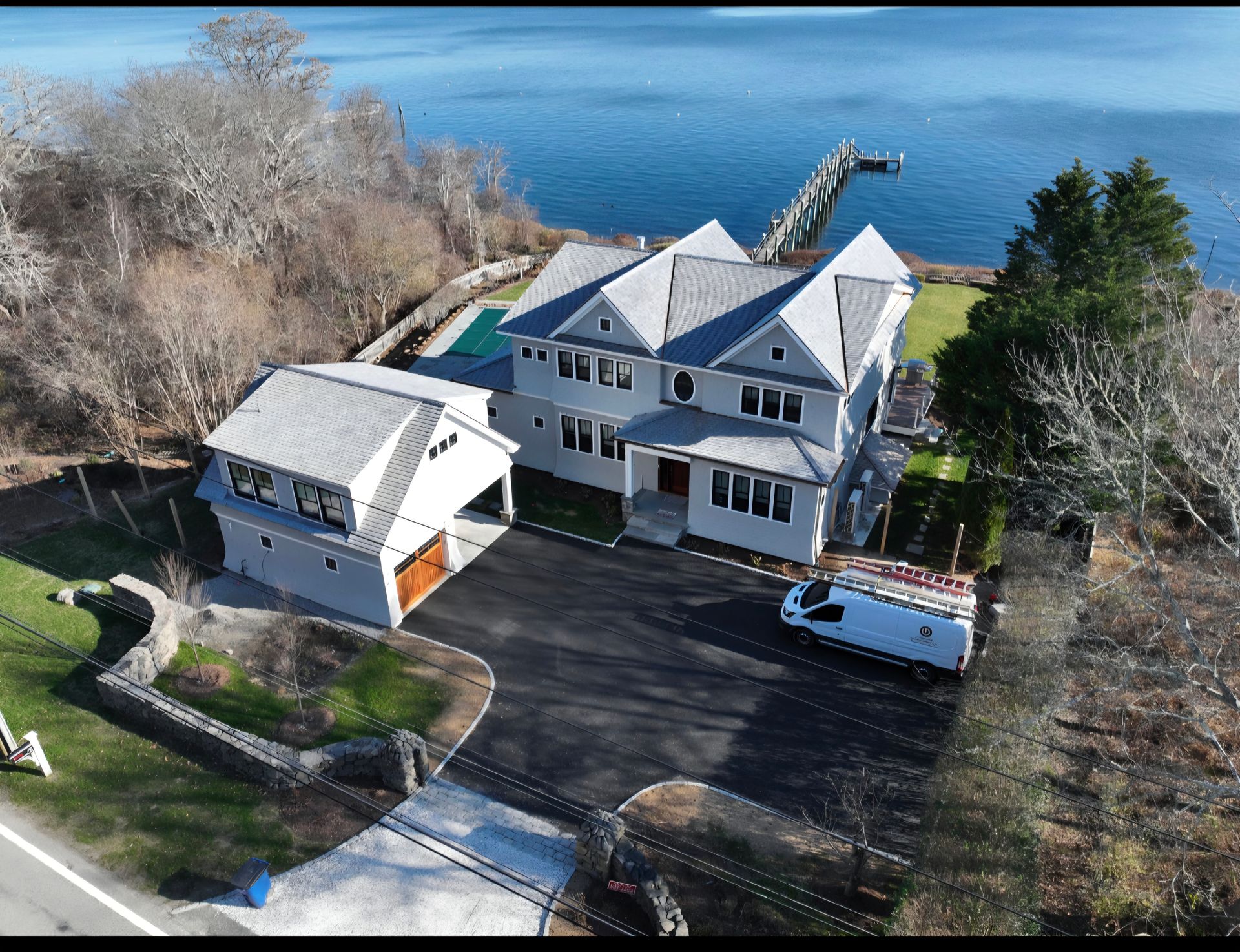 Large gray house with water views, driveway, attached garage, and pier.