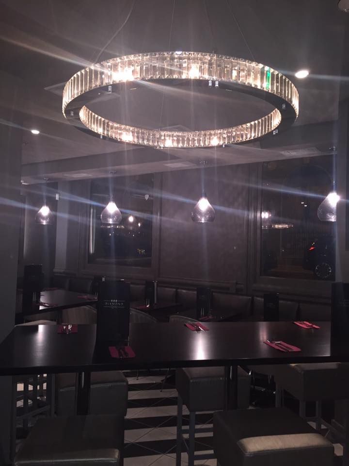 Two-story blue house with stone columns, large windows, and a balcony, set on a grassy lawn.