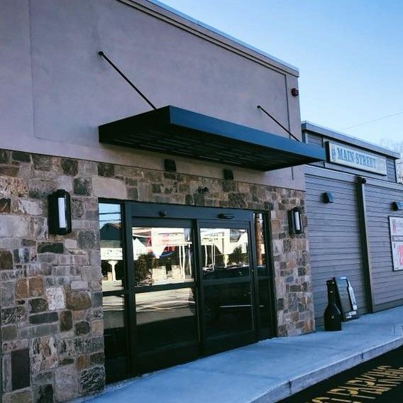 A white crane truck with its arm extended upward between tall brick and stone buildings under a bright blue sky.