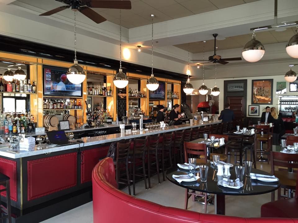 A crane lifts a large, mirrored bottle between two historic brick buildings under a blue sky.