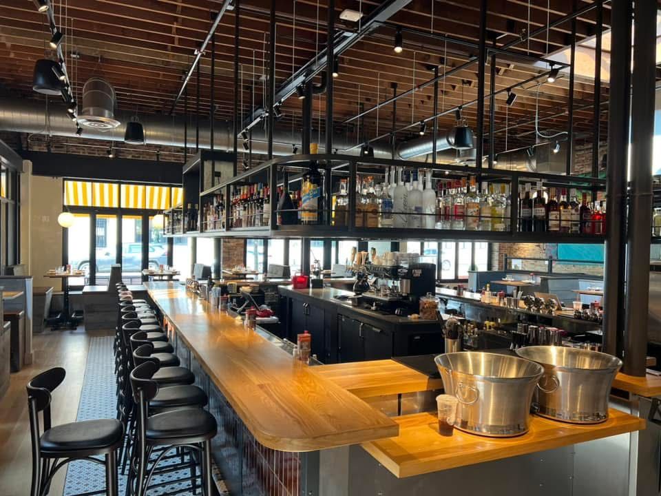 Interior of a bar with a long wooden counter, stools, and a liquor display overhead