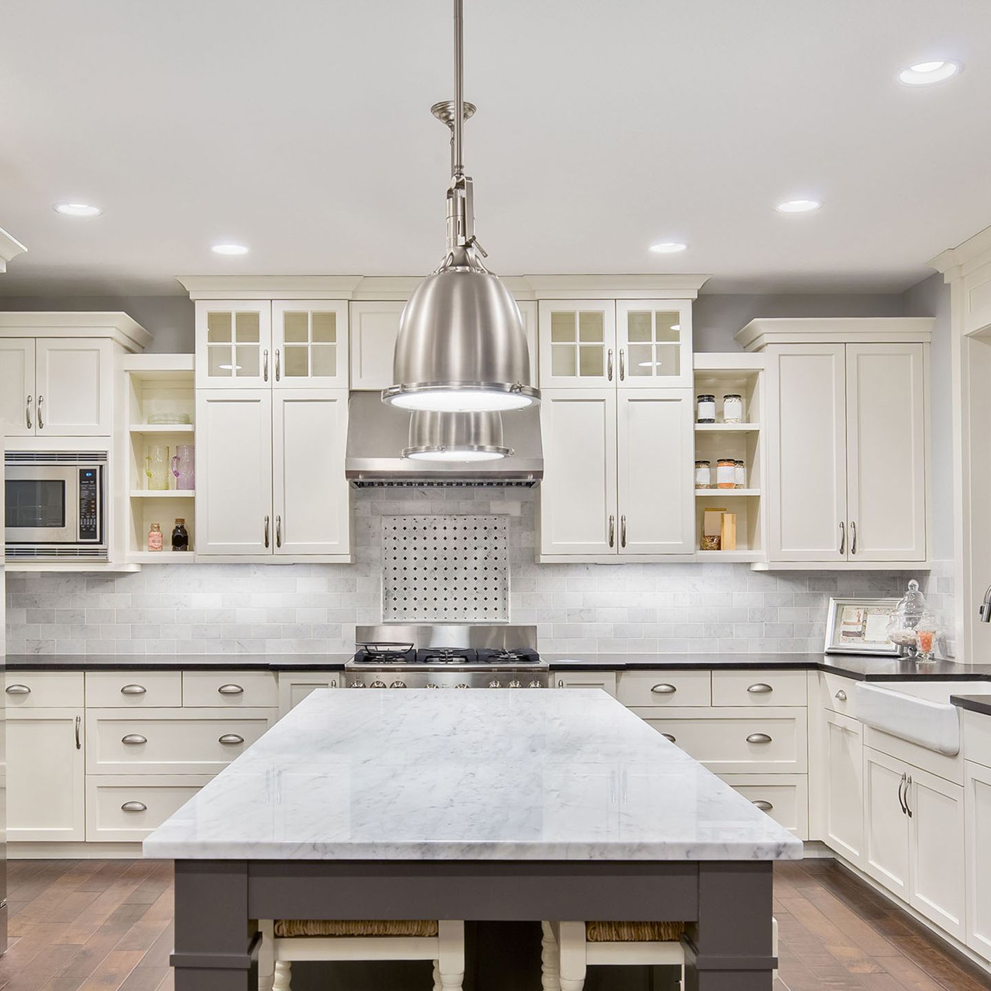White kitchen with a marble-topped island, stainless steel appliances, and white cabinets.