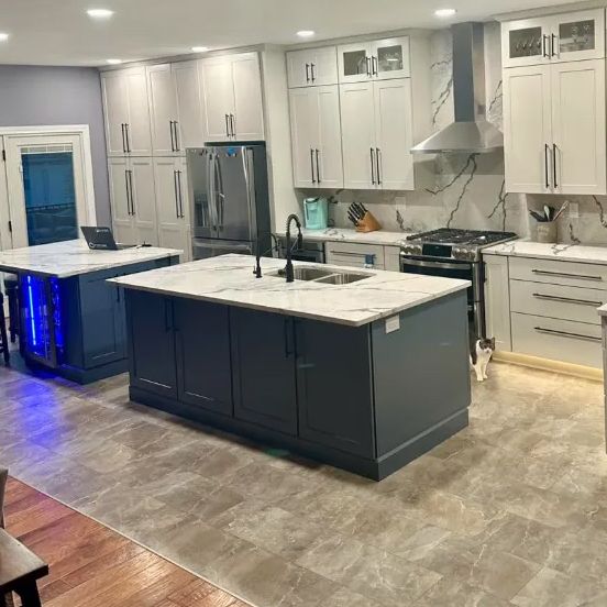 Modern kitchen with two dark blue islands, white cabinets, stainless steel appliances, and marble countertops.