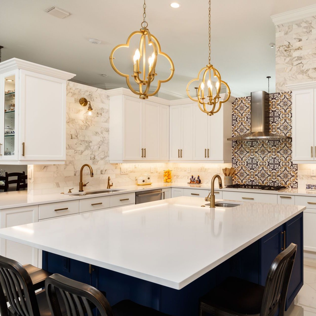 Kitchen with white cabinets, blue island, gold light fixtures, and patterned backsplash.