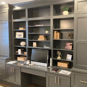 Gray built-in home office with desk, shelves, and cabinets; items on shelves include plants, books, and decor.
