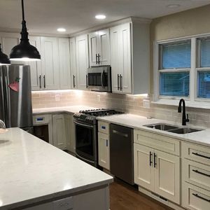 White kitchen with stainless steel appliances, dark hardware, and pendant lights.