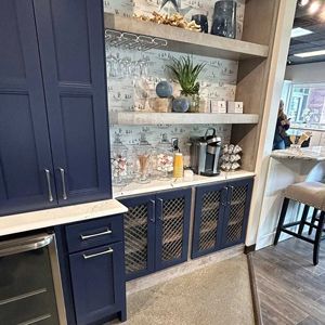 Navy blue cabinetry with marble countertop. Built-in shelving with coffee station, glassware, and decor.