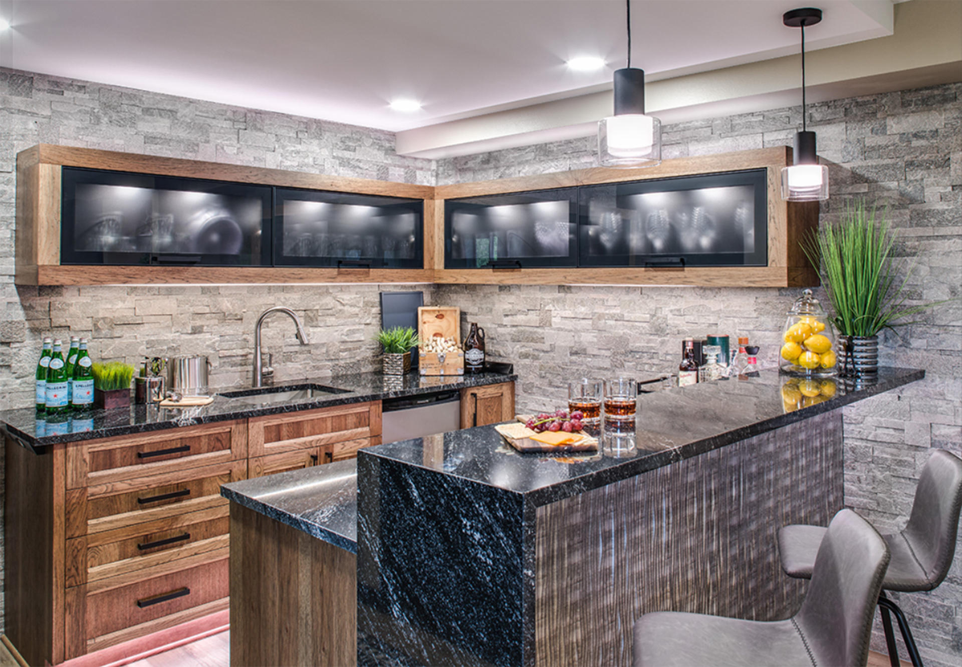A kitchen with a bar, sink, cabinets, and a brick wall.