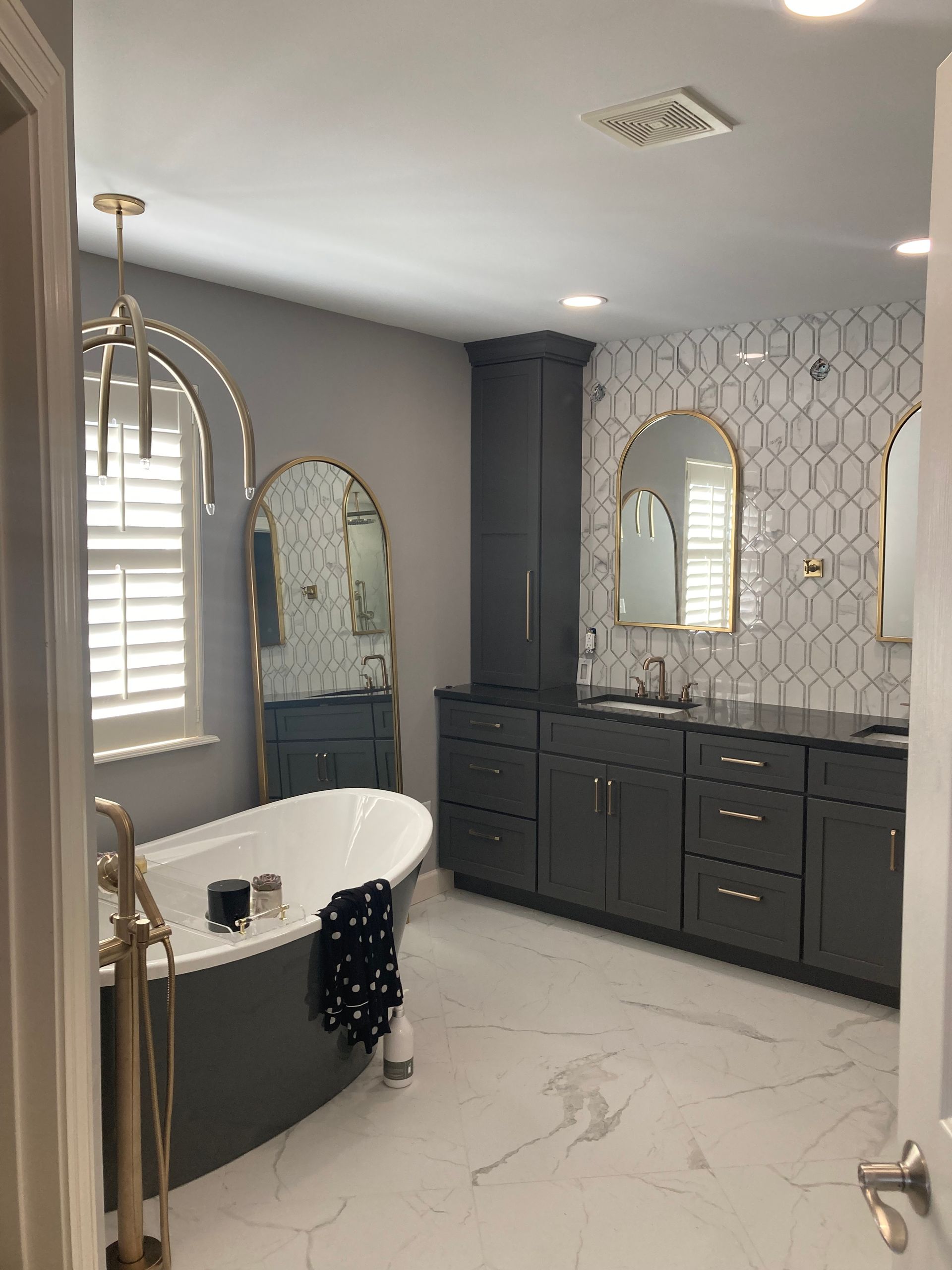 A bathroom with a tub , sink , mirrors and cabinets.