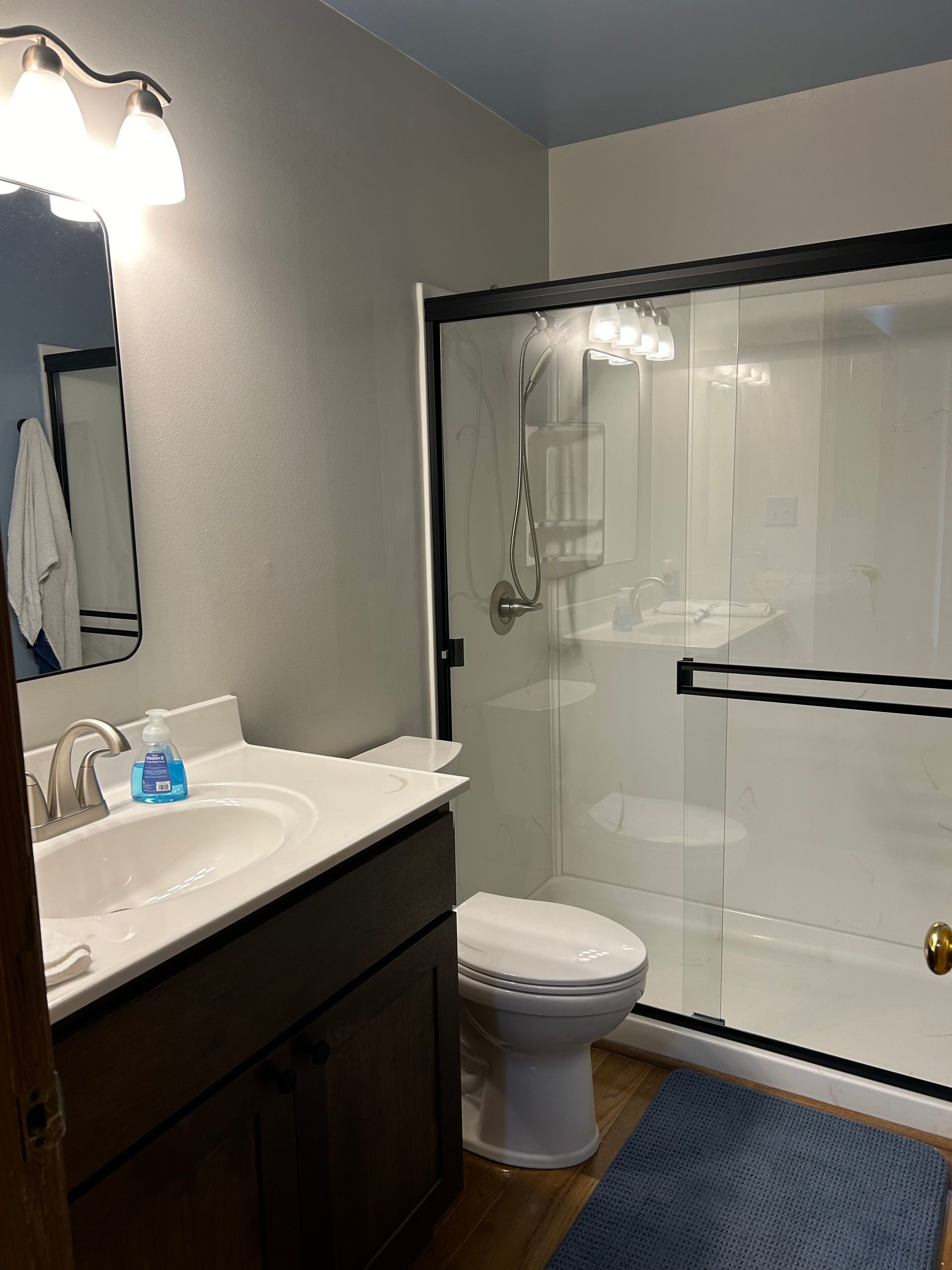 A bathroom with a toilet , sink , mirror and shower.
