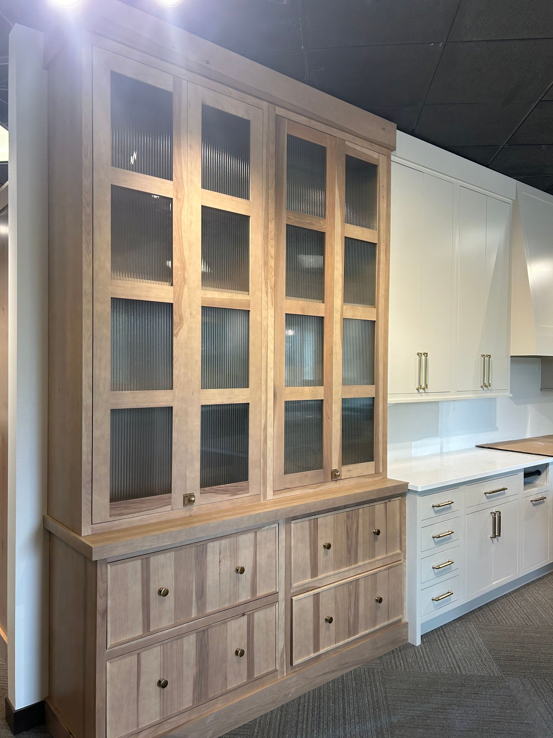 A kitchen with white cabinets and wooden cabinets with glass doors