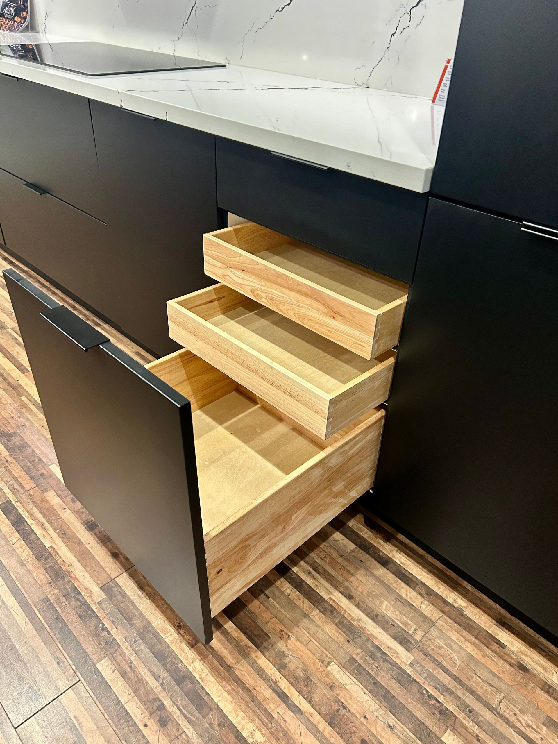 A kitchen with black cabinets and wooden drawers.