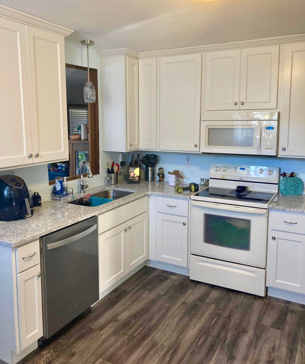 A kitchen with white cabinets , a stove , a microwave , and a sink.