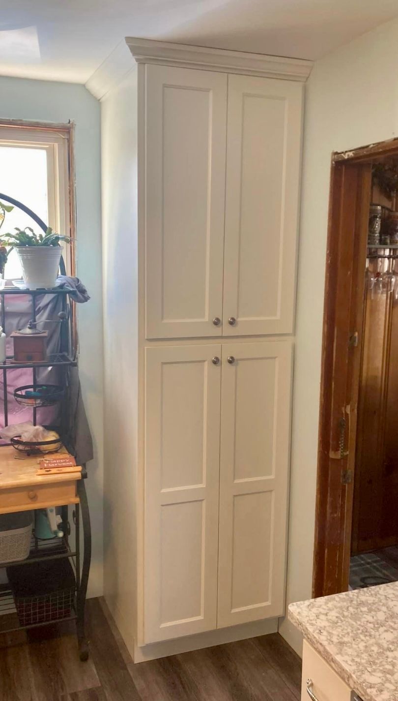A tall white cabinet in a kitchen next to a window.