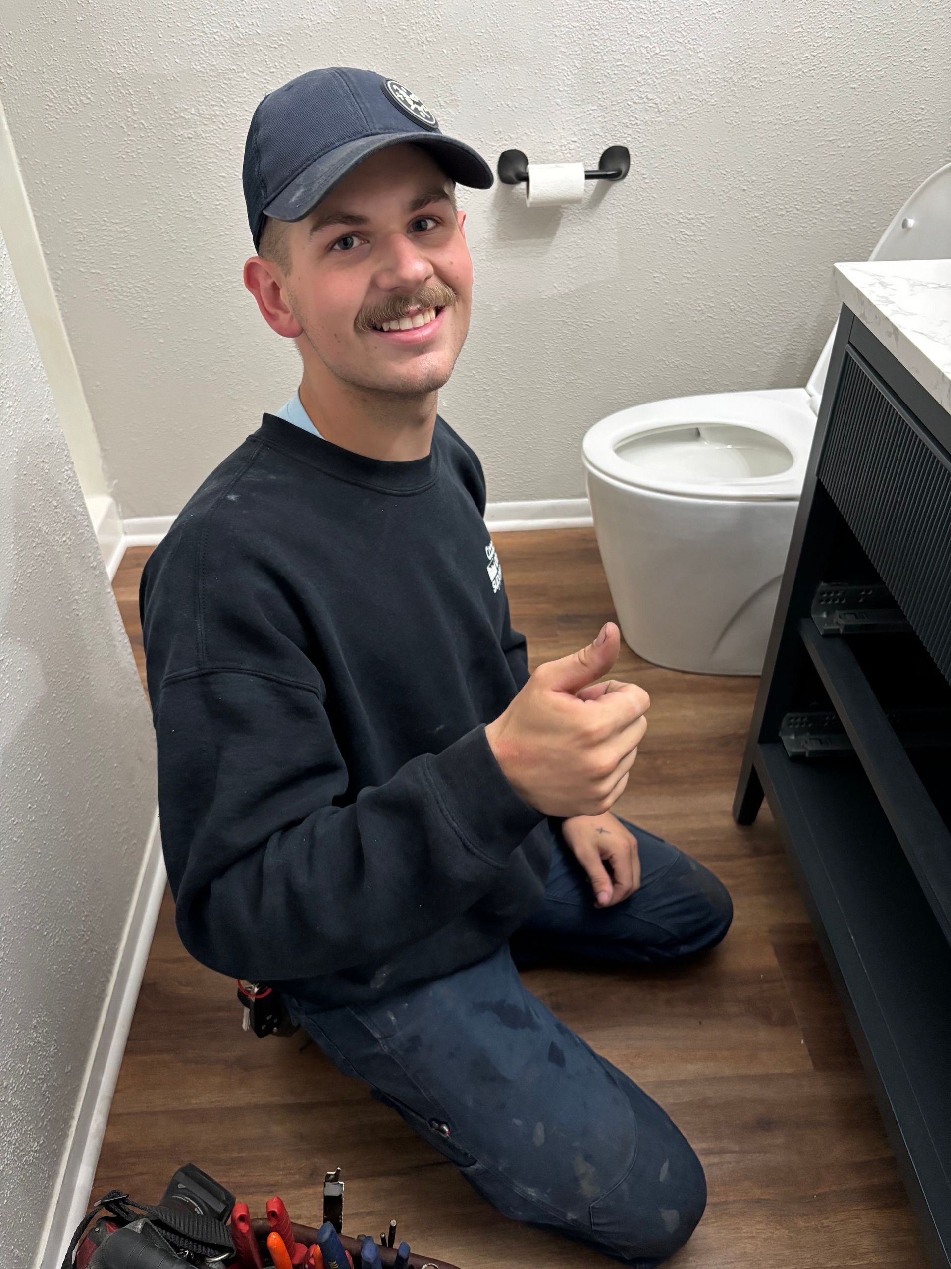 Zachary Strong sitting on the floor in a bathroom, giving a thumbs-up to the camera
