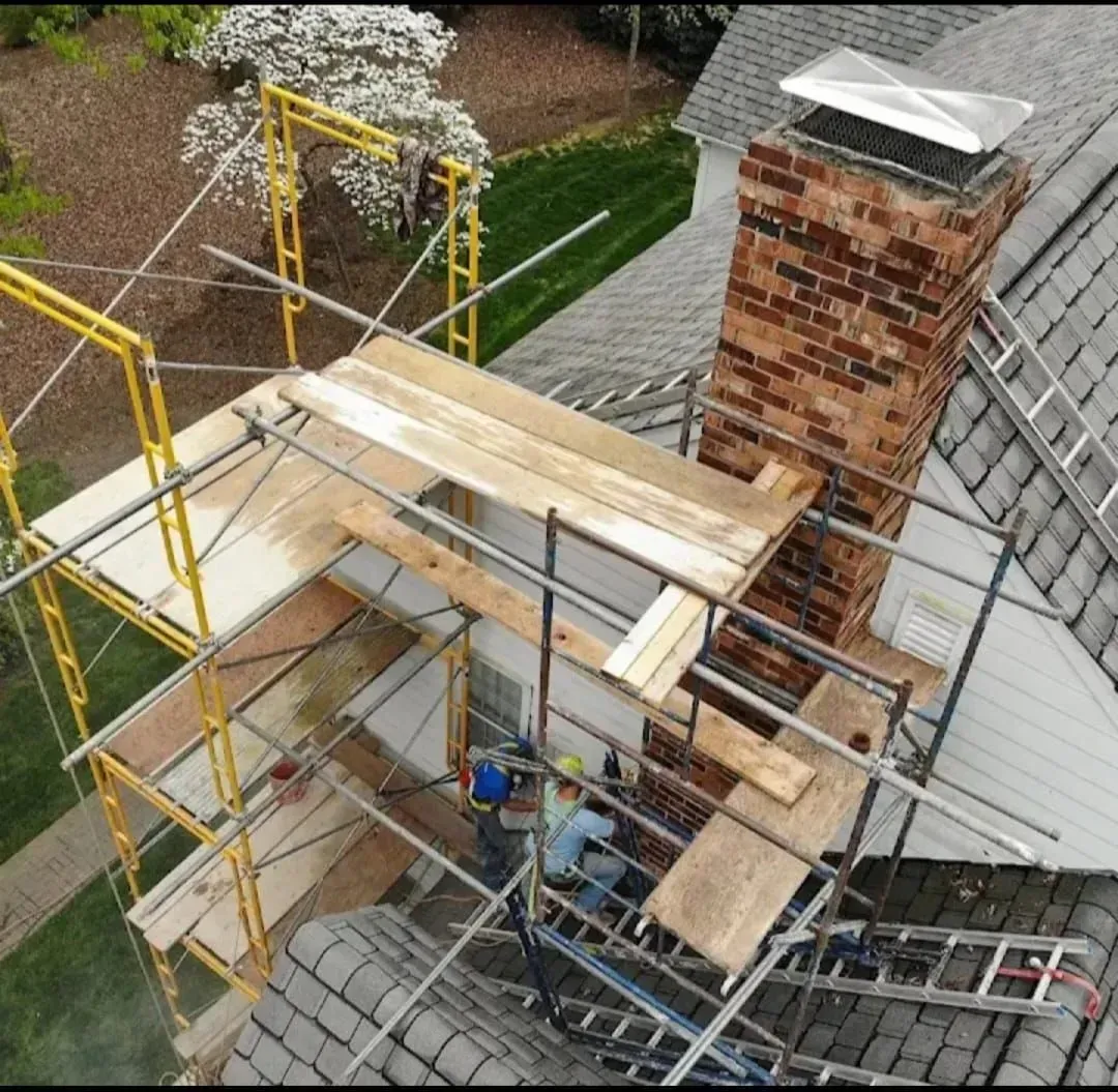 Roof repair scaffolding beside brick chimney on a gray shingled house