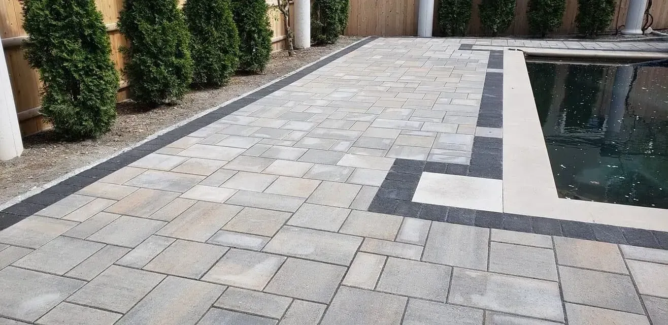 Stone patio beside a reflecting pool with geometric gray pavers and hedges along the left side.