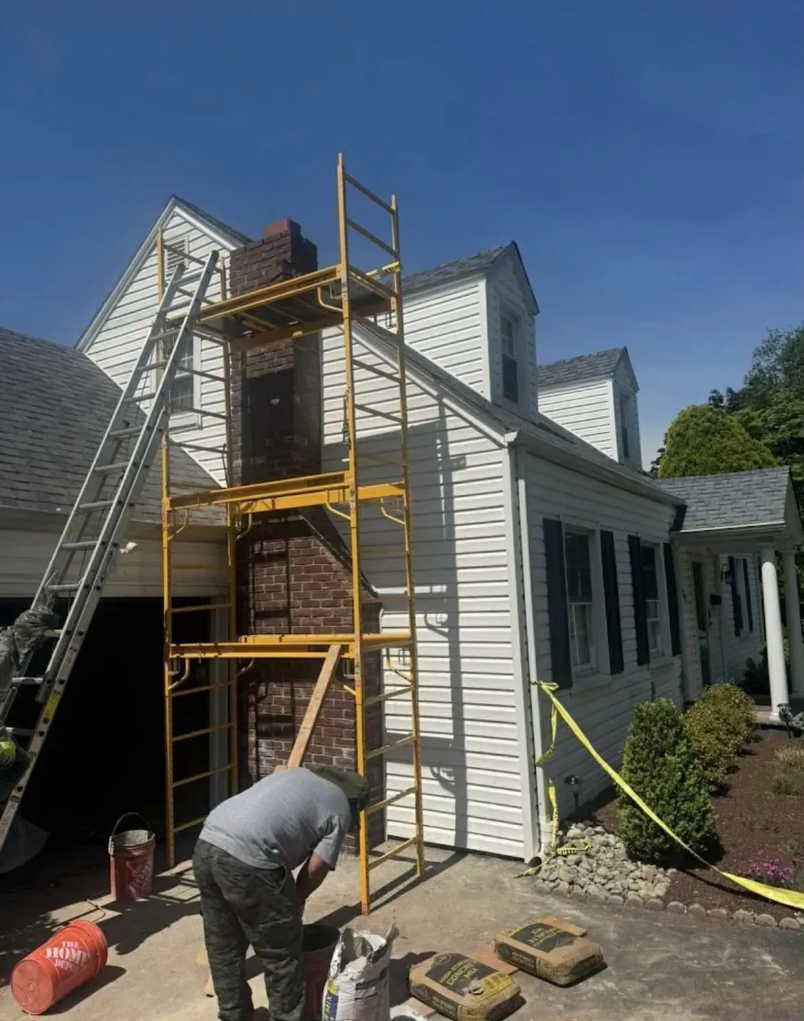 Worker on a ladder and scaffold painting a white house exterior during repairs