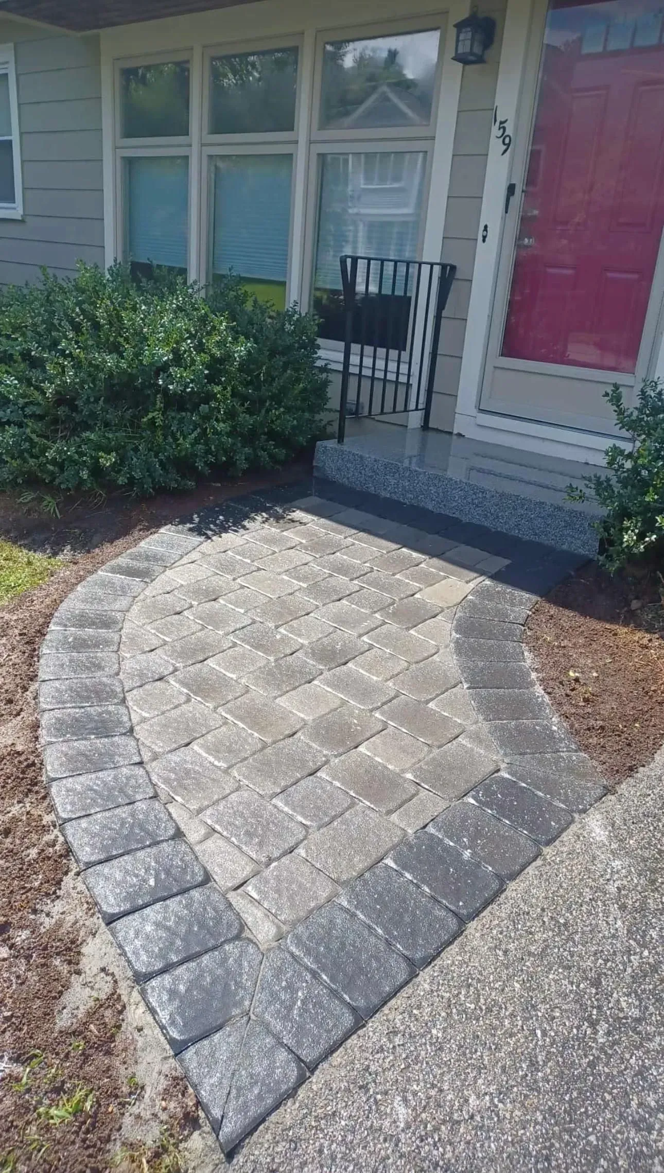 Curved stone walkway leading to a front porch with white railing, windows, and a red door panel