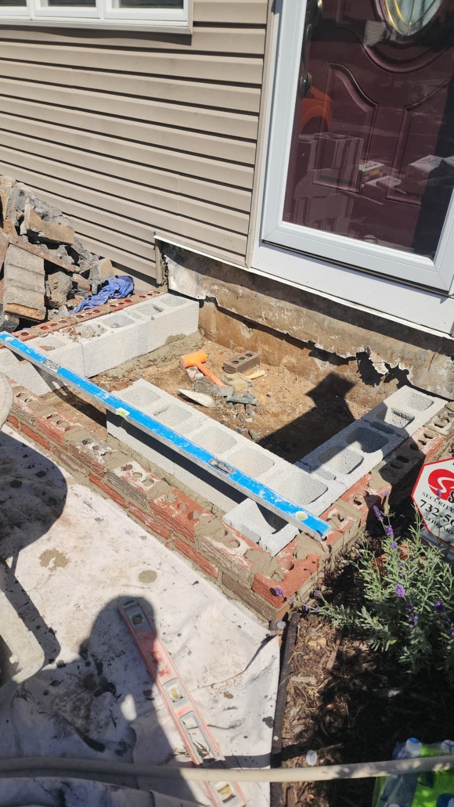 Construction site: cinder block and brick border around sunken area near a door. A blue level sits atop the blocks.