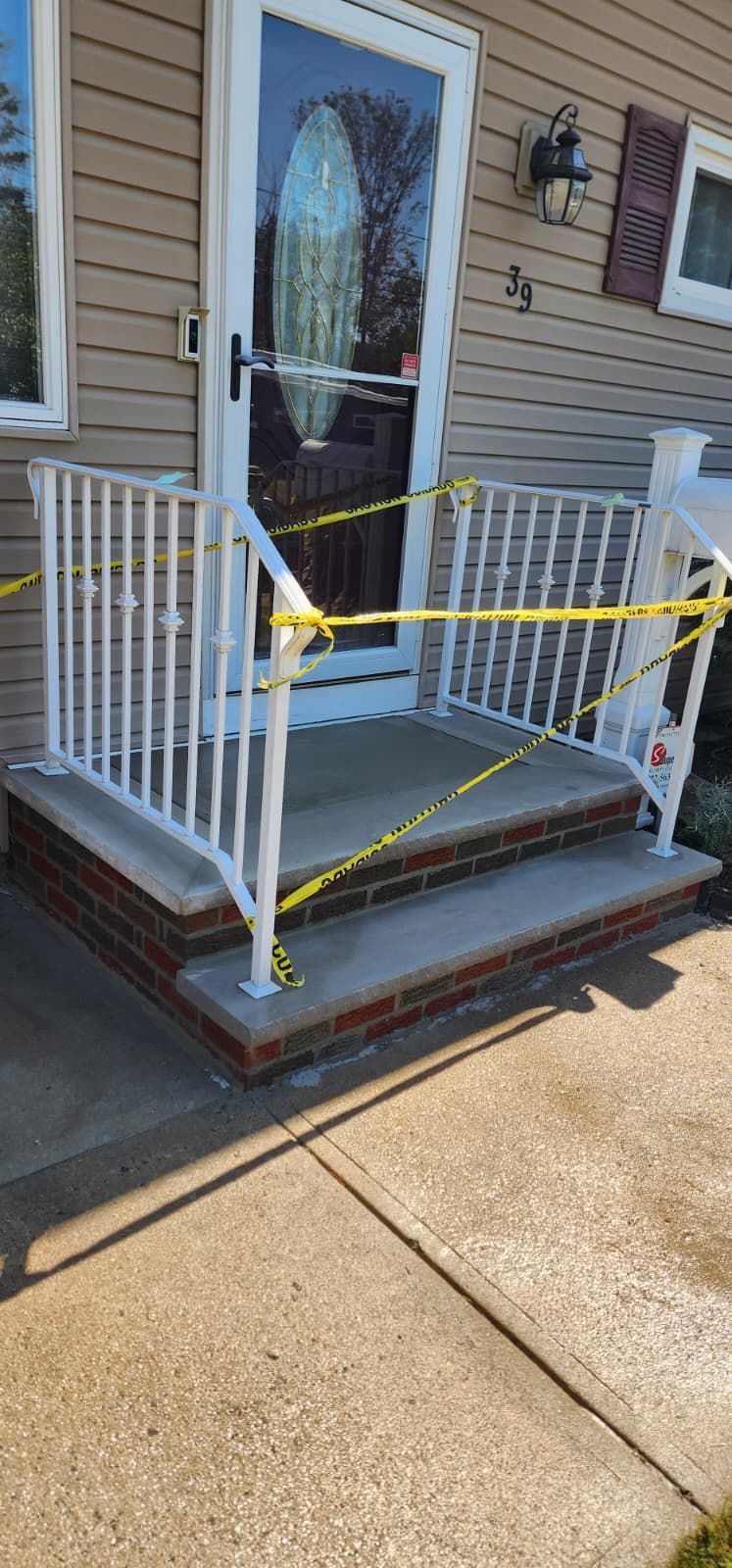 Exterior view of a house with a concrete porch and steps, white railing, and a yellow caution tape, indicating possible danger.