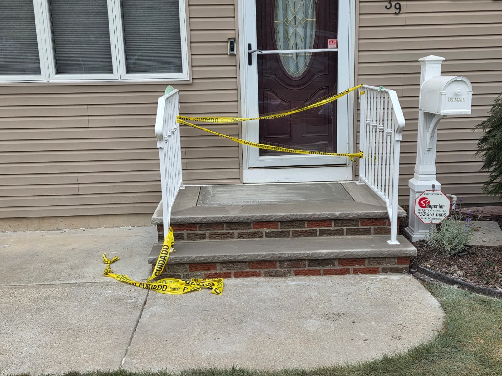 Yellow caution tape blocks steps to a front door with white railings. A mailbox is to the right.