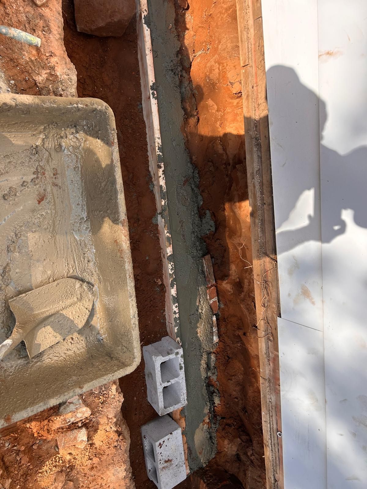 Trench with wet concrete, cinder blocks, and a mortar tray, ready for brickwork.