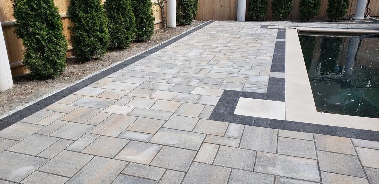 Patio with pavers, landscaping, and a pool. The pavers are gray.