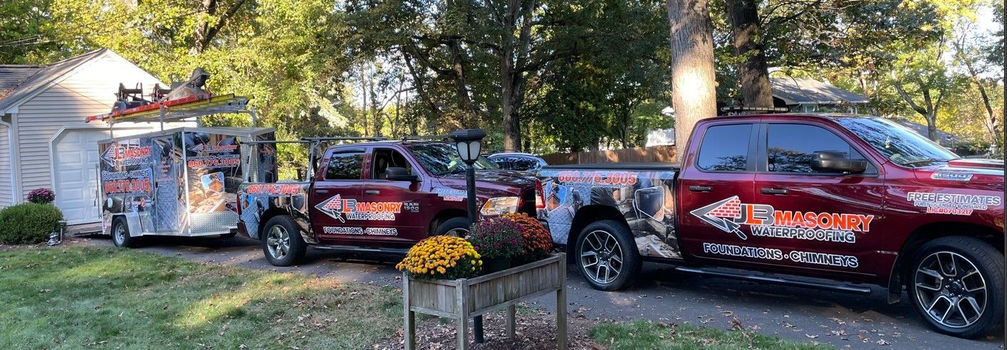 Red trucks and trailer in a yard with business logo on the side, in front of a house.