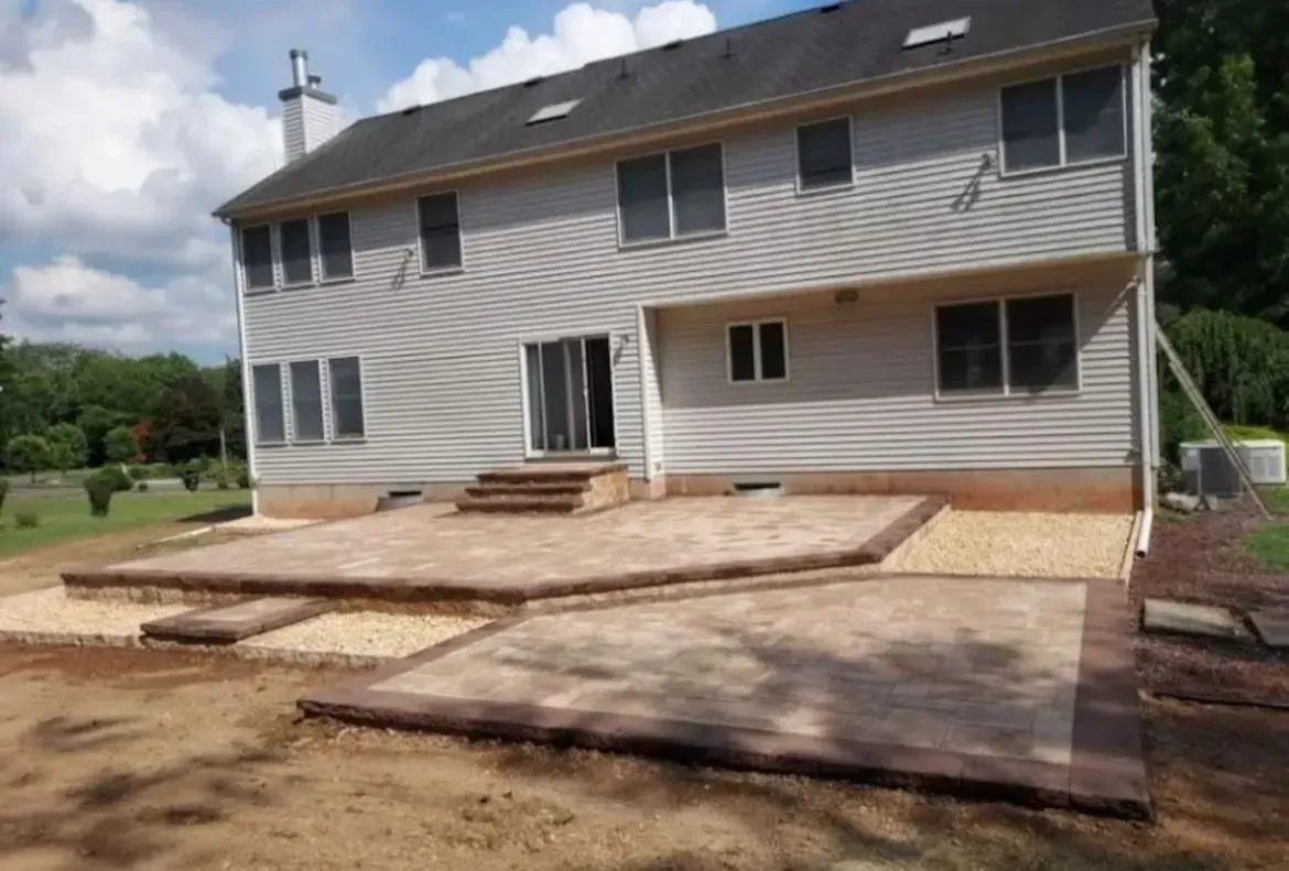 Two-story house with a newly poured concrete patio and steps in a muddy yard