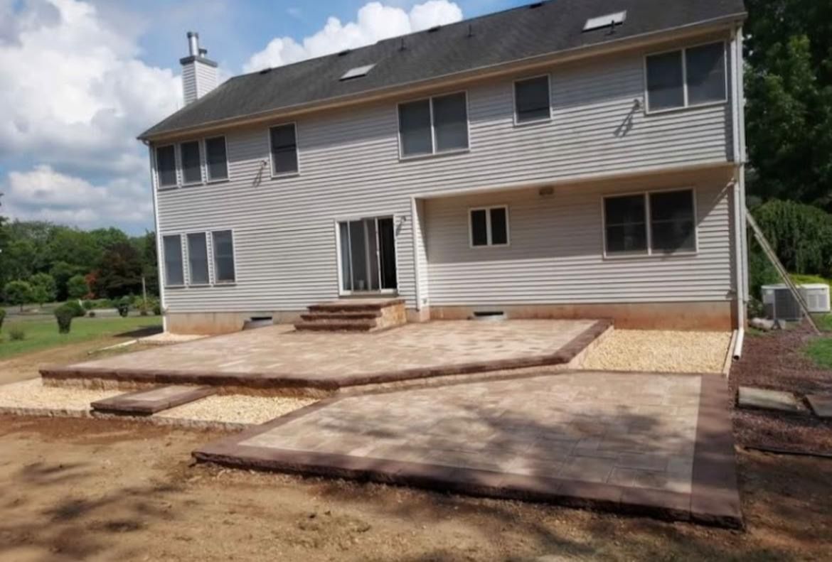 Back of a two-story house with a newly constructed patio. Beige pavers, gravel border, brown trim.