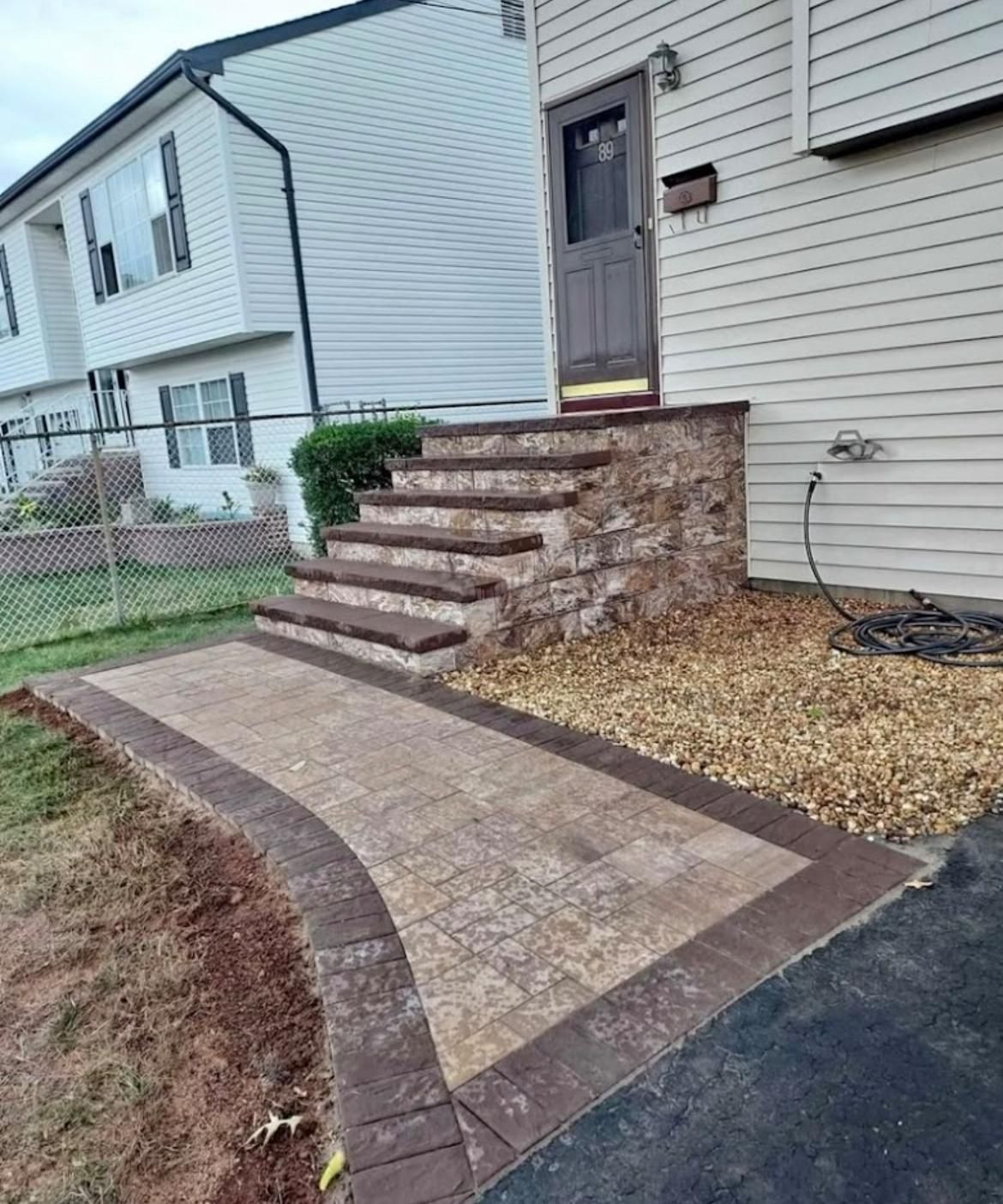 Brick walkway and steps leading to a house entrance with tan siding, a brown door, and gravel.