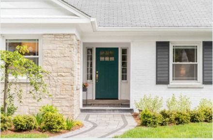 Front porch of a house with a teal front door, stone facade, and curved walkway through a small lawn