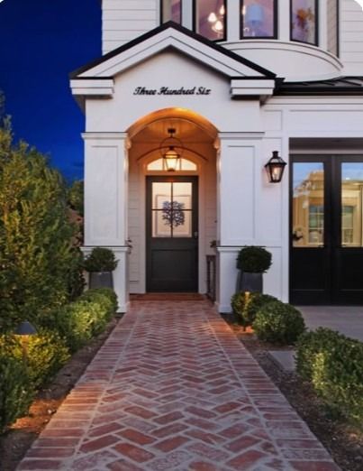 Brick walkway leads to a lit, white building entrance with arched doorway at dusk.