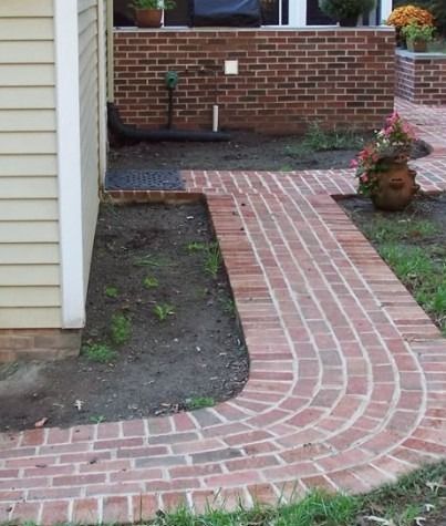 Brick walkway curving through a small garden bed beside a house and brick wall