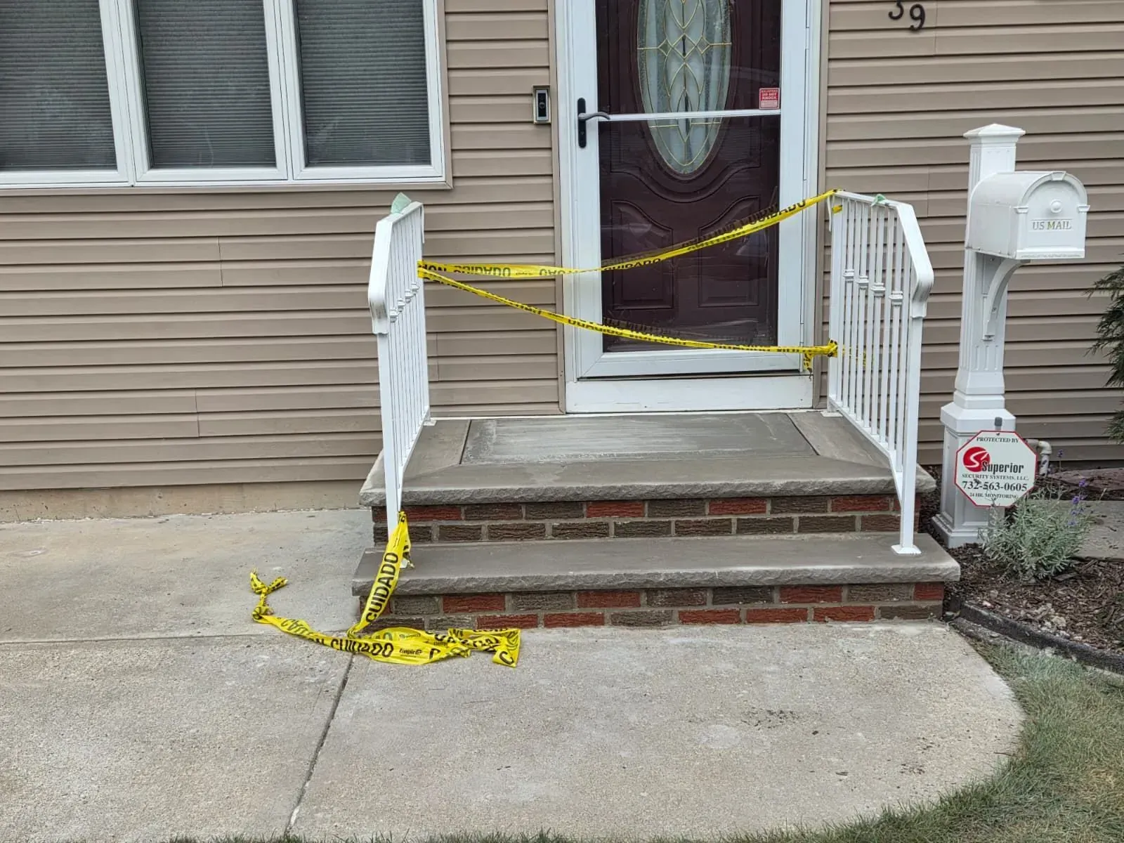 Front porch blocked with yellow caution tape, red brick steps, and a white railing beside a front door.