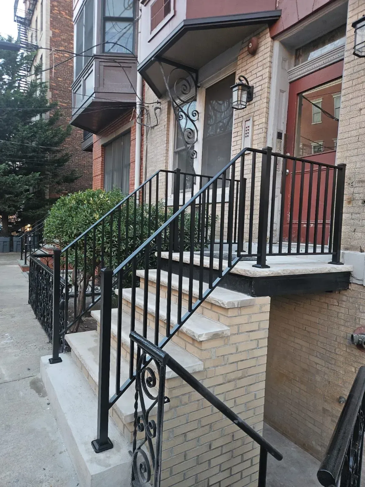 Front stoop of a brick townhouse with black railings and stairs leading to a doorway