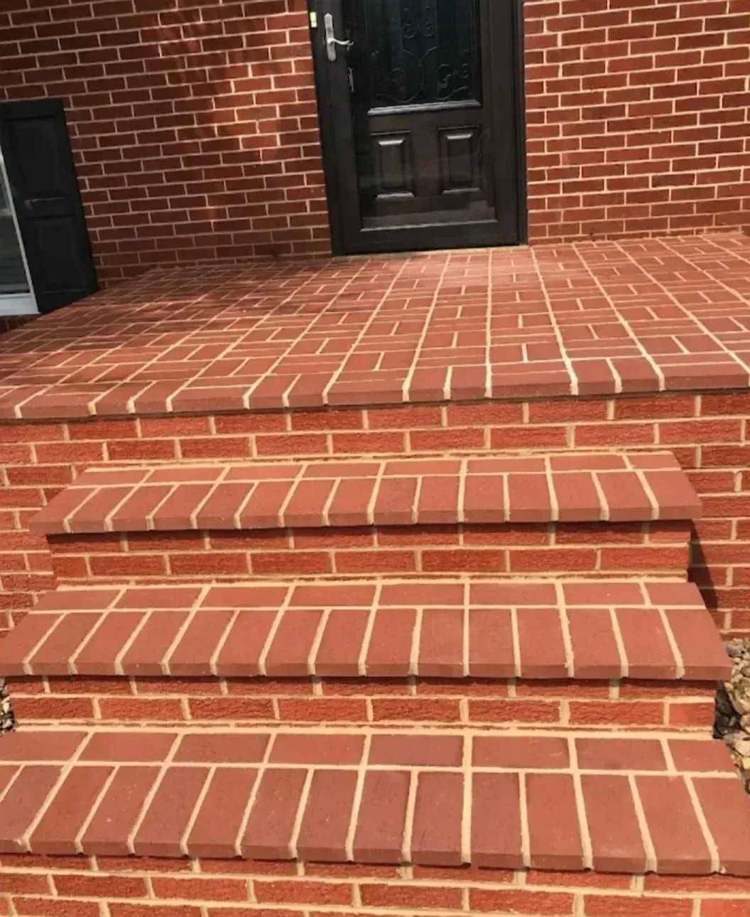 Brick front steps leading to a dark wooden door on a brick house