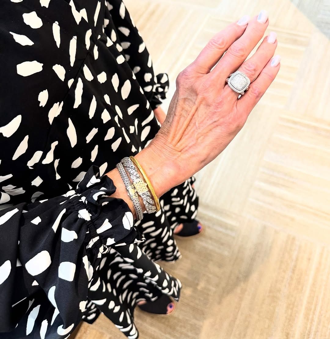Woman's hand with large ring and bracelets, wearing a black and white patterned top.
