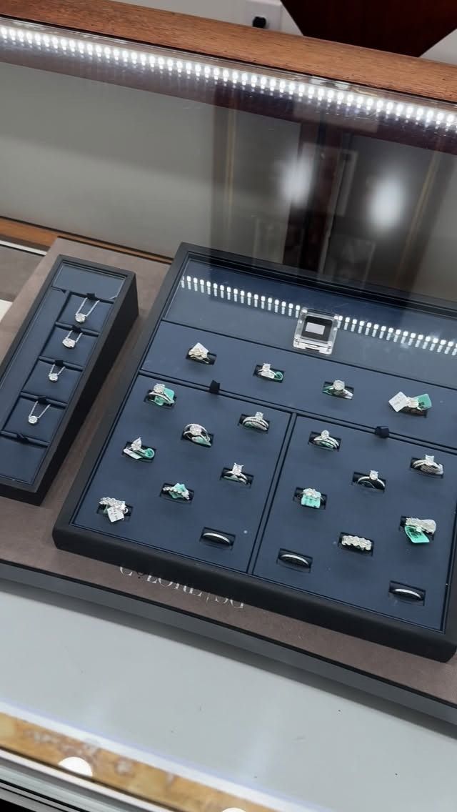Jewelry display case with various rings on black velvet trays, under bright lights.