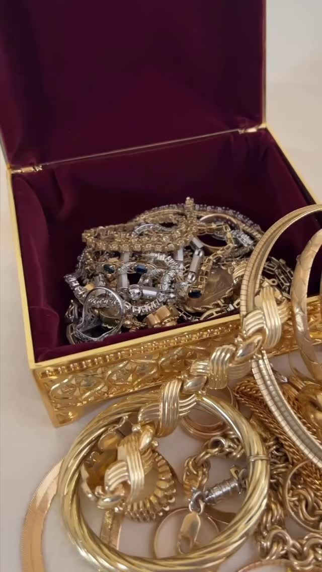 Gold jewelry spilling from an ornate box lined with maroon velvet.