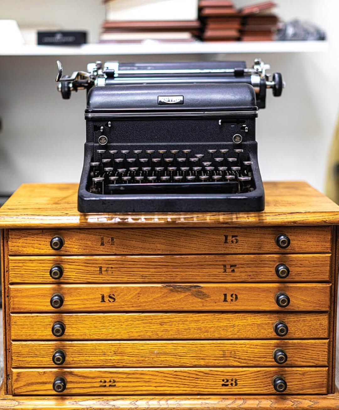 Black typewriter on a wooden drawer set, lit by soft lighting.