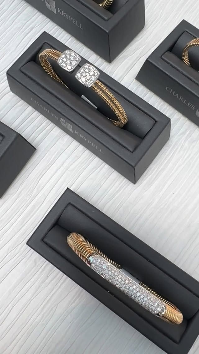Jewelry display: gold and diamond bracelets in black boxes on a white surface.