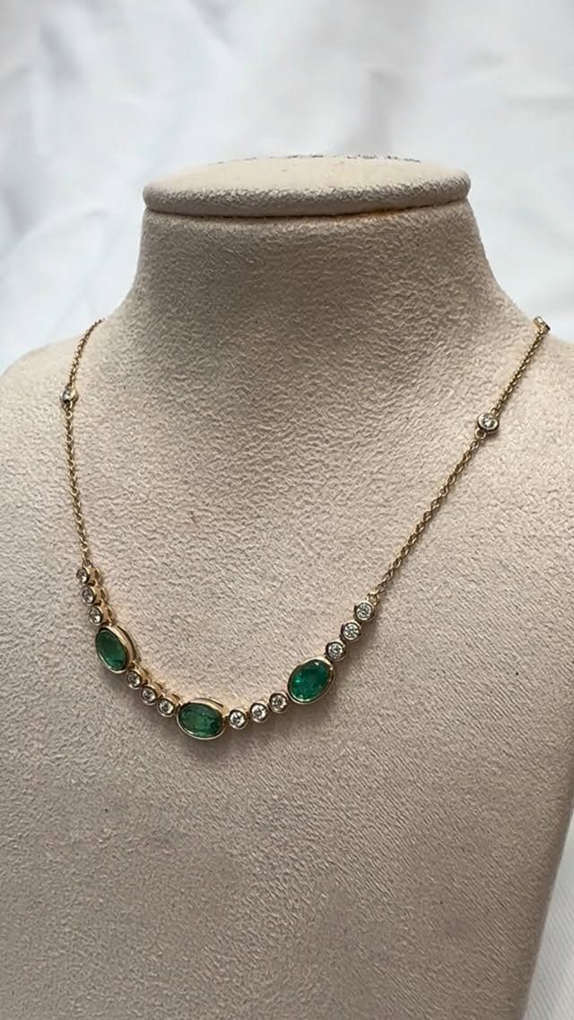 Gold necklace with oval green stones and small diamonds displayed on a mannequin.
