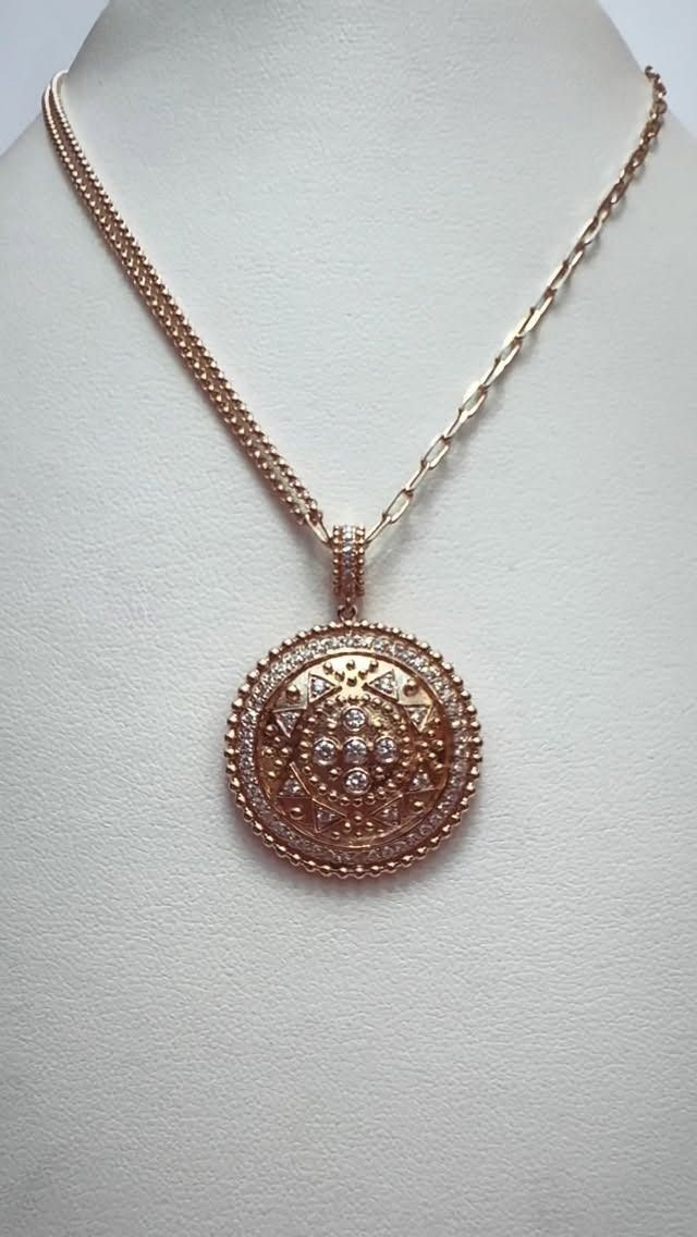 Rose gold pendant necklace with a round, jewel-encrusted medallion, displayed on a white surface.