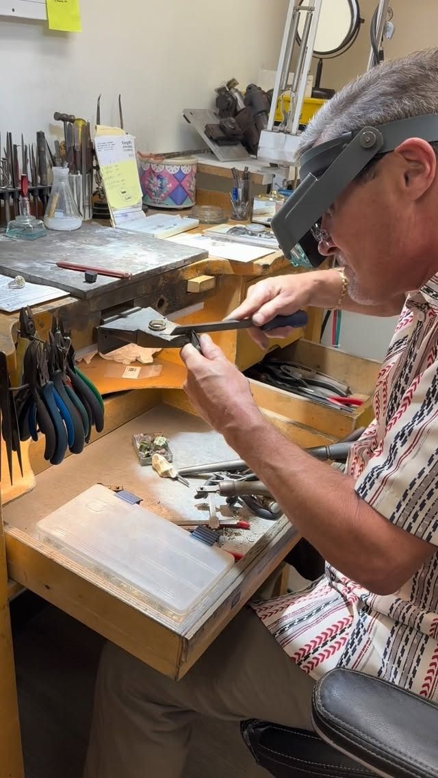 A person working with small tools at a workbench. They are wearing a magnifying visor and focusing on a small object.